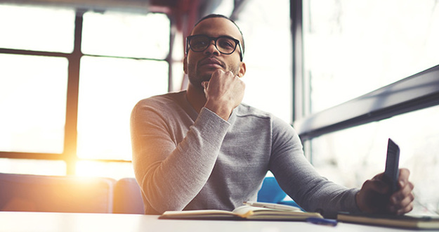 Consider This Before Defining Your Investment Philosophy young African American male sitting in cafe with open book on table and head resting on hand thinking