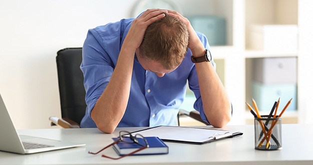 This Could Devastate Your Real Estate Investing Business seated man looking down with hands on back of head and elbows on desktop worried, sad or frustrated at work