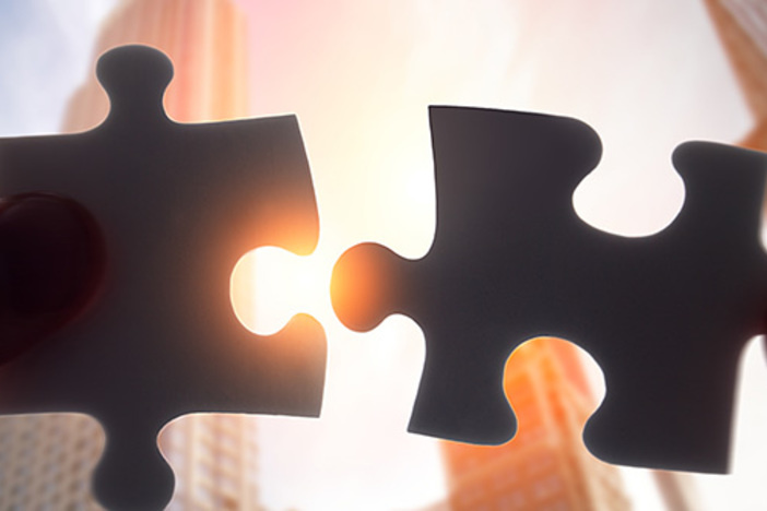 Insurance or Asset Protection: Which is Best for Investors? two puzzle pieces about to be fit together with blurred cityscape in backdrop