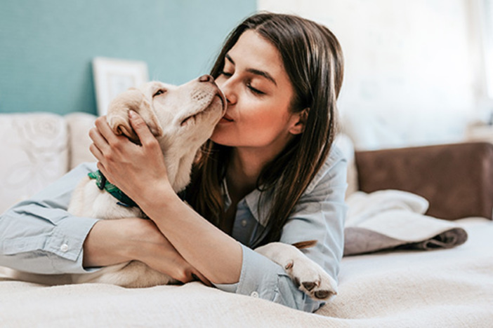 Should You Allow Pets in Your Rentals? woman laying on bed snuggling light colored big dog