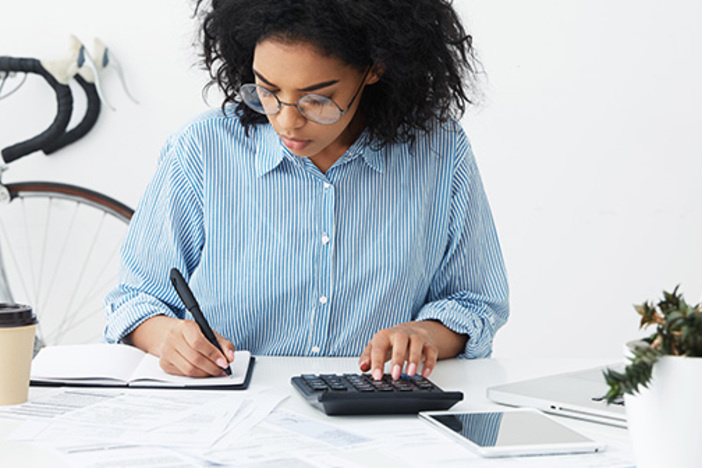 1031 Exchange: What Investors Should Know About Closing Costs businesswoman doing paperwork at office desk, working through finances, using calculator and making notes in her notebook with pen