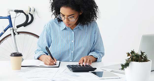 1031 Exchange: What Investors Should Know About Closing Costs businesswoman doing paperwork at office desk, working through finances, using calculator and making notes in her notebook with pen