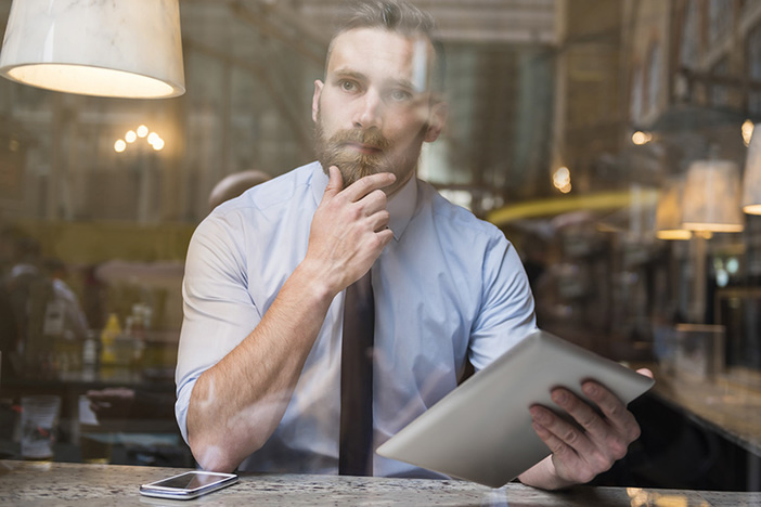 True or False: Commercial Real Estate Is Guaranteed to Perform Better Than Stocks white main behind window sitting at table with phone and tablet and inquisitive expression