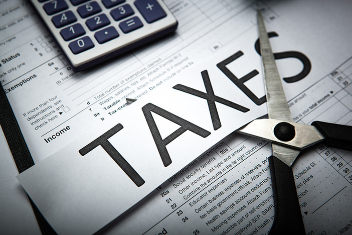8 Ways to Maximize Your 2020 Tax Benefits as a Real Estate Investor tax forms and calculator on desk taxes written in large font on slip of paper scissors preparing to cut it