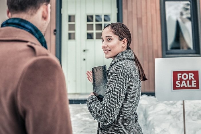 Real Estate Agents: Avoid These 9 Missteps To Maintain Your Motivation and Close More Deals Smiling realtor greeting her customers outside the house for sale in winter with snow on ground