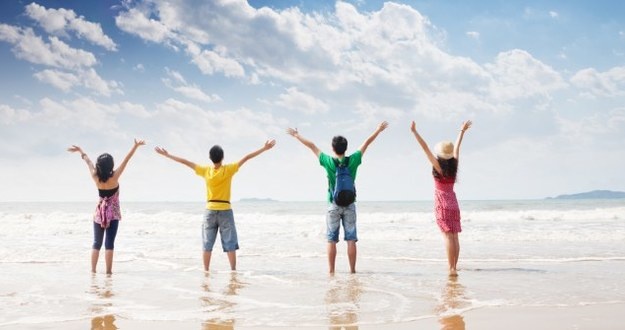 How to Jointly Buy a Vacation Home Without Destroying a Friendship four people on beach in colorful clothing facing ocean with arms in air