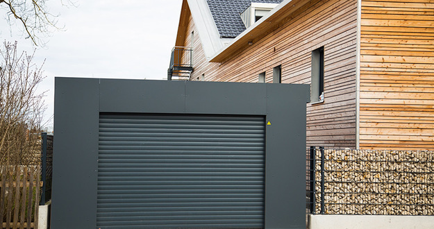 Why Investing in Garages Is an Ideal Way to Create Passive Income detached garage painted black with black garage door next to a modern looking house with natural wood siding exterior