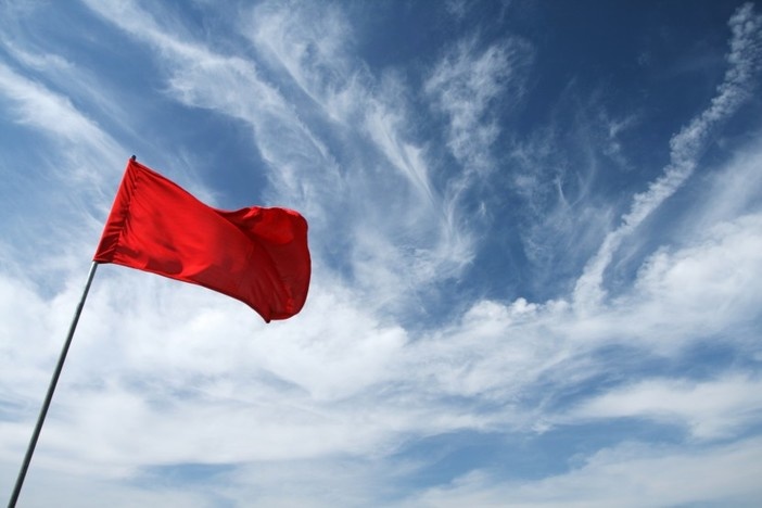 10 Glaring Red Flags That Indicate Your “Great Deal” May Be a Costly Scam blue sky background with some clouds and red flag in foreground waving in wind