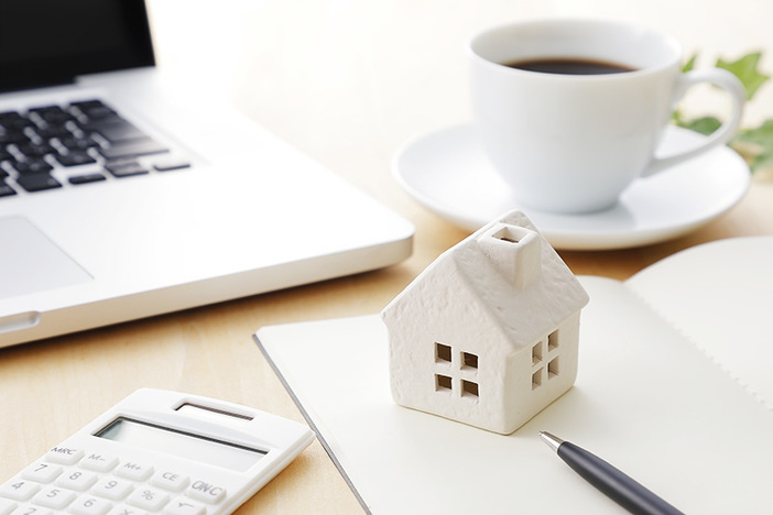 So, You Just Bought a Real Estate Note? Here’s What to Expect Next. wooden model of house on desk with coffee cup, calculator, laptop
