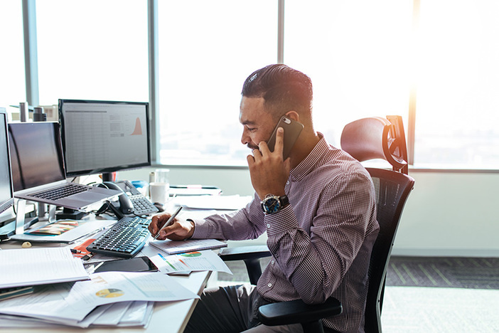 How to Become an Entrepreneur: 4 Vital Tips for Success Businessman talking on mobile phone and making notes. Man sitting at his office desk working on graphs and charts and discussing on phone.