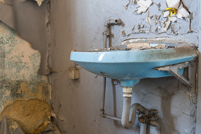 A Video Tour of My Rental From Hell: What Went Wrong & What I’m Doing to Fix It old blue bathroom sink with exposed pipes in trashed bathroom with peeling gray walls and holes in the wall